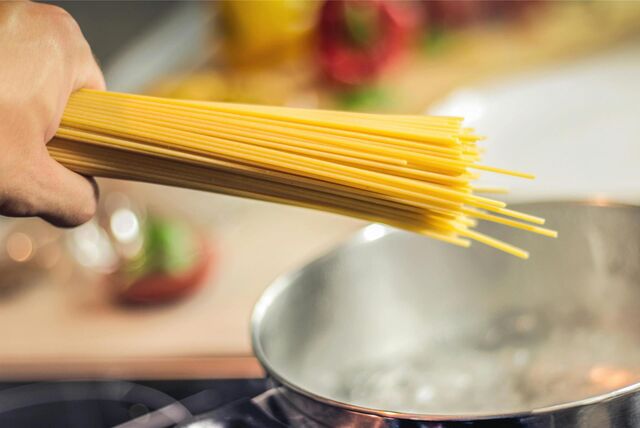 Eine Person hält rohe Spaghetti über einen Topf mit kochendem Wasser.