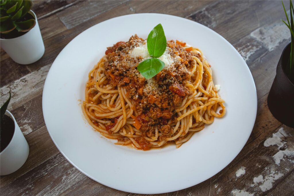 Ein Teller mit einer Portion Spaghetti Bolognese steht auf einem Tisch. Ein Teller mit einer Portion Spaghetti Bolognese steht auf einem Tisch.