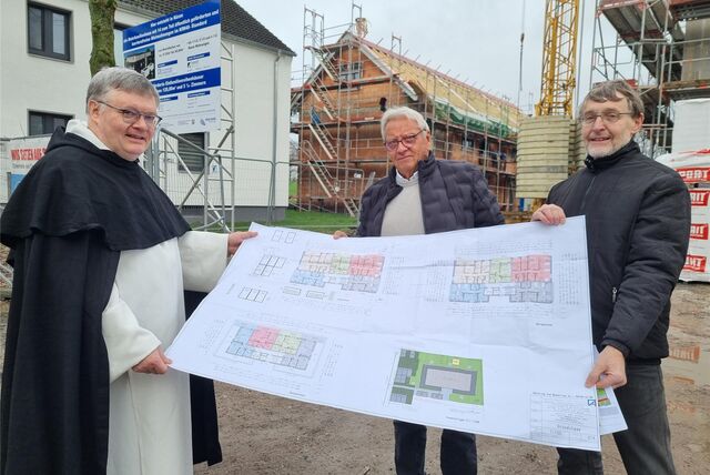 Drei Männer halten einen Bauplan vor zwei Neubauten.
