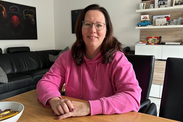 Eine Frau im pinken Pulli sitzt am Esstisch.