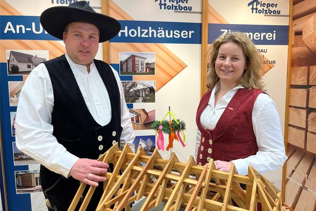 Mann und Frau in traditioneller Zimmermannskluft vor einem Modell eines Dachstuhls