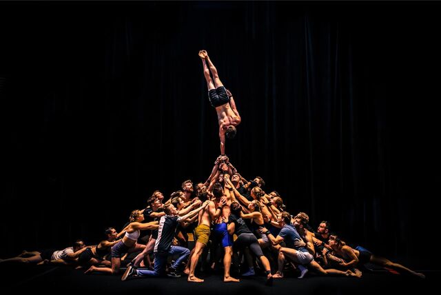 Eine Zirkus-Performance mit vielen Menschen, die eine Person im Handstand heben.