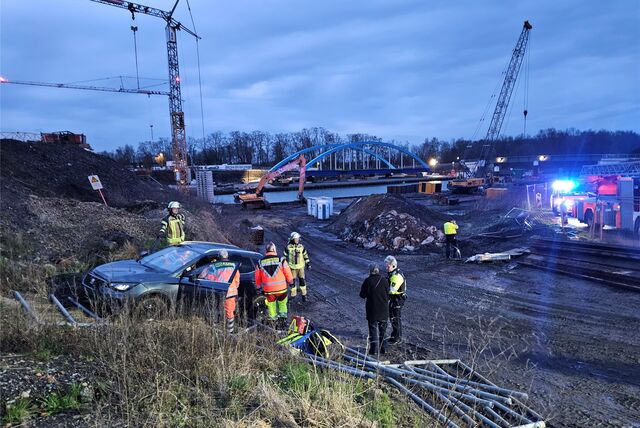 Feuerwehrleute stehen an einem Auto in einer Baustelle.
