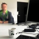 Eine Person sitzt an einem Schreibtisch. Die Person ist verpixelt.
