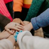 Mehrere Personen stehen im Kreis und halten die Hände in der Mitte übereinander. Sie symbolisieren Zusammenhalt.