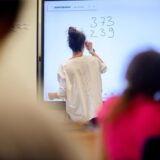 Eine Lehrerin schreibt etwas an ein Whiteboard.