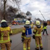 Feuerwehrleute stehen vor einer großen Rauchwolke an einer Gewerbeimmobilie in Herten-Süd.