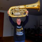 Gerd Kluth aus Marl steht in einem Probenraum der Musikschule Recklinghausen, er hebt eine Tuba in die Luft.