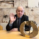 Mark Gutkin ist Vorsitzender der jüdischen Kultusgemeinde für den Kreis Recklinghausen. Für seine ehrenamtliche Arbeit erhielt er den Ehrenpreis für Gesellschaft und Kultur der Stadt Castrop-Rauxel. Gutkin lacht und winkt in die Kamera. Vor ihm steht die Auszeichnung.