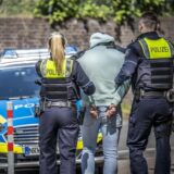Ein Polizist und eine Polizistin führen einen gefesselten Mann zum Streifenwagen.