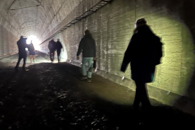 Mehrere Menschen gehen durch einen Tunnel, sie sind von hinten als Schattenrisse zu erkennen. Am Ende des Tunnels ist Tageslicht zu erkennen.