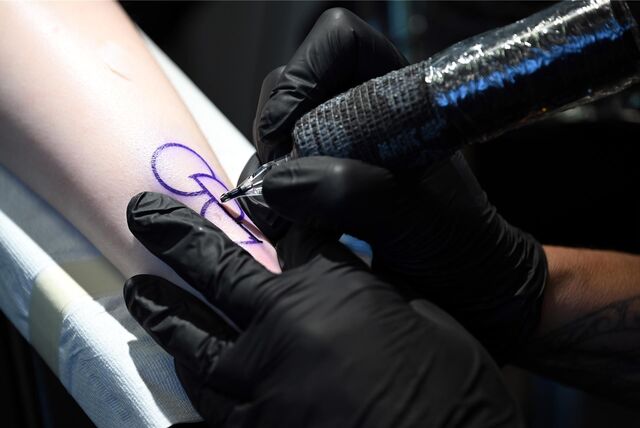 Eine Tattoo-Künstlerin tätowiert zwei Halbkreise und einen ganzen Kreis auf einen Unterarm.