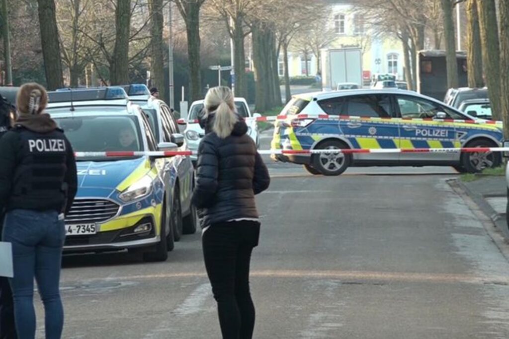 Einsatzkräfte der Polizei stehen vor Absperrband auf einer Straße in Ochtrup. Einsatzkräfte der Polizei stehen vor Absperrband auf einer Straße in Ochtrup.
