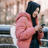 Eine Frau mit einem Kopftuch guckt auf ihr Handy.