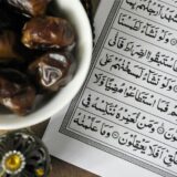 Eine Schale mit Datteln steht auf einem Tisch, daneben liegt ein muslimisches Gebetbuch.