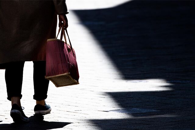 Eine Frau hält eine Handtasche in ihrer Hand, sie läuft auf einer Straße auf einen überschatteten Bereich zu.