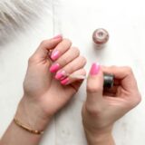 Eine Frau mit pinkfarbener Maniküre trägt einen glitzernden Topcoat auf.