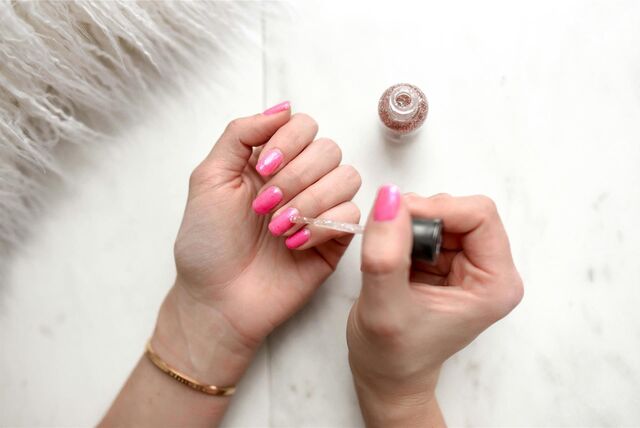 Eine Frau mit pinkfarbener Maniküre trägt einen glitzernden Topcoat auf.