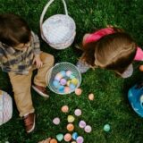 Zwei Kinder sitzen auf einer Wiese und betrachten die gesammelten Ostereier in ihren Körben.