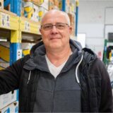 Kai-Uwe Drees steht neben einem hohen Regal mit gefüllten Kartons.