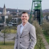 Immobilienmakler Michael Dschaak steht draußen, hinter ihm ein Blick auf Castrop-Rauxel und den Erin-Turm.
