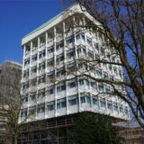 Das Marler Rathaus von schräg unten. Der Turm im Hintergrund ist mit Gerüsten umgeben. Der Turm im Vordergrund nur unten am Sockel. Der Himmel im Hintergrund ist wolkenlos blau.