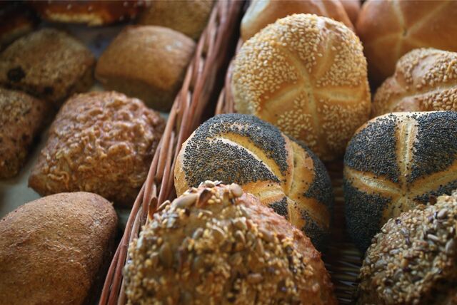 Verschiedene mit Körnern bedeckte Brötchen liegen in der Auslage eines Bäckers.