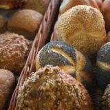 Verschiedene mit Körnern bedeckte Brötchen liegen in der Auslage eines Bäckers.