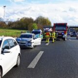 Ein verbeulter Pkw, Rettungsfahrzeuge und Polizeibeamte stehen auf der Autobahn, während der Verkehr auf der anderen Fahrspur vorbeigeführt wird.