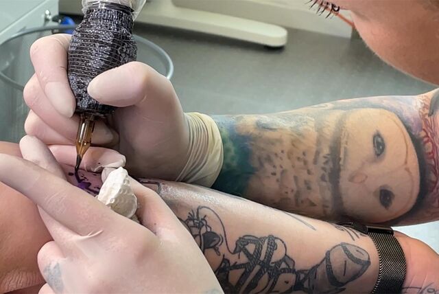 Eine Tätowiererin verziert den Arm eines Tattoo-Trägers mit dem Symbol für die Organspende.