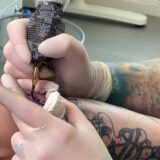 Eine Tätowiererin verziert den Arm eines Tattoo-Trägers mit dem Symbol für die Organspende.