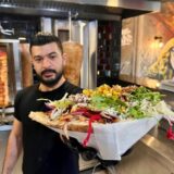 Ein Mann hält in einem Döner-Imbiss vor zwei Drehspießen einen fertigen Döner in der Hand.