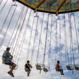 Menschen sitzen auf einer Kirmes in einem Kettenkarussell.