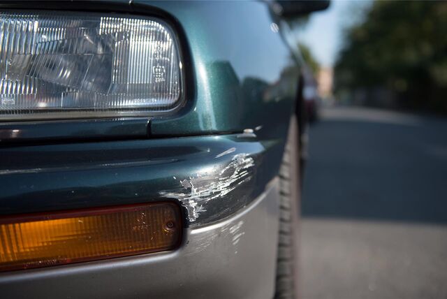 An der Vorderschürze zerstörtes Auto, das parkt, daneben Blick auf eine lange Straße.