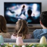 Ein Mann, eine Frau und ein kleines Mädchen sitzen an Ostern vor dem Fernseher und genießen das TV-Programm.