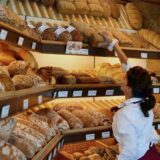 Eine Verkäuferin greift in einer Bäckerei und Konditorei in den Auslagen des Geschäfts nach einem Brot aus dem reichhaltigen Angebot.