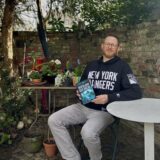 André Winkler aus Recklinghausen sitzt mit seinem Buch „Klang der Rache“ an einem weißen Tisch im Garten.