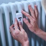 Eine Frau kontrolliert einen Heizkostenverteiler an der Heizung.