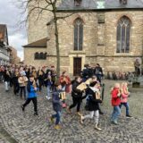 Kinder und Jugendliche mit Räppeln ziehen um eine Kirche in Waltrop.