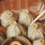 Teigtaschen, auch Dumplings genannt, liegen in einer Schale und werden mit Stäbchen gegessen.