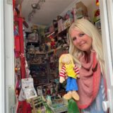 Nici van Grote schaut mit einer Puppe in der Hand durch die Tür ihres Kindergeschäfts „Lilly & Loui“! in Dortmund.