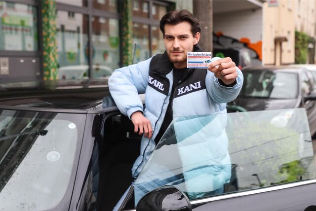 Ein Mann steht in Dortmund vor einem Mini Cooper D und hält die Karte eines Autohändlers in die Kamera.