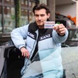 Ein Mann steht in Dortmund vor einem Mini Cooper D und hält die Karte eines Autohändlers in die Kamera.