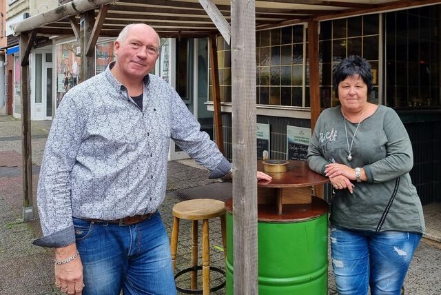Ein Mann und eine Frau stehen an einem Stehtisch vor einer Kneipe.