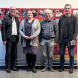 Carsten Löcker, Kathrin Timm, Stephan Schüppen und Dr. Frank Lelke (von links) stehen in der Christy-Brown-Schule  vor einer Wand voller Schüler-Fotos.
