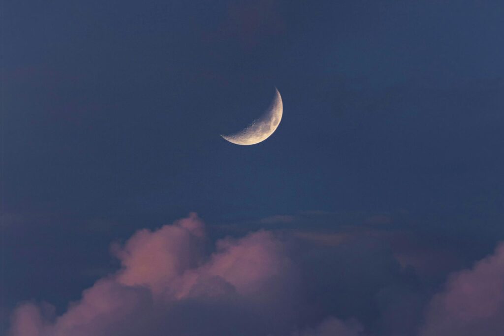 Eine Sichel des Mondes ist am Abendhimmel über einer Wolke zu sehen.
