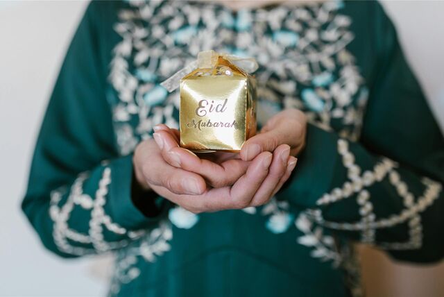 Eine muslimische Frau hält ein Geschenk zum Zuckerfest mit der Aufschrift „Eid Mubarak“ in der Hand.
