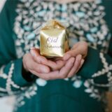 Eine muslimische Frau hält ein Geschenk zum Zuckerfest mit der Aufschrift „Eid Mubarak“ in der Hand.