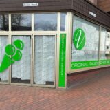 Die Außenansicht einer Eisdiele. Die Fenster sind von innen mit Papier verhangen, sodass man nicht hineinschauen kann. Am Außenglas ist in Grün eine große Eistüte und der Name des Eiscafés geklebt.