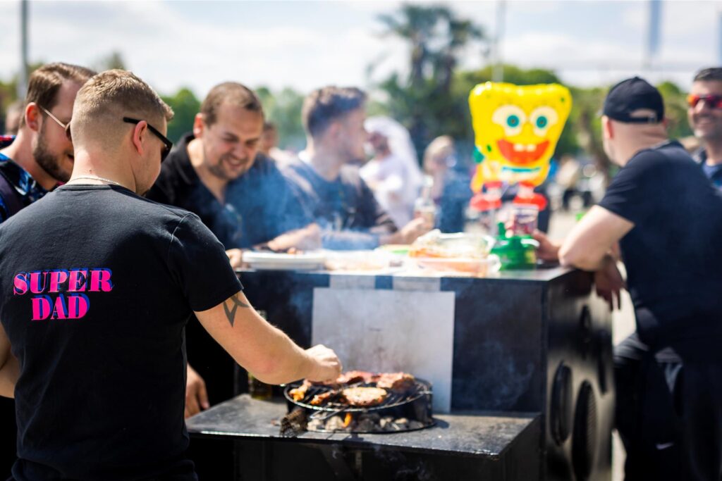 Ein Mann grillt am Vatertag an einem Bollerwagen, an dem seine Freunde stehen. Ein Mann grillt am Vatertag an einem Bollerwagen, an dem seine Freunde stehen.